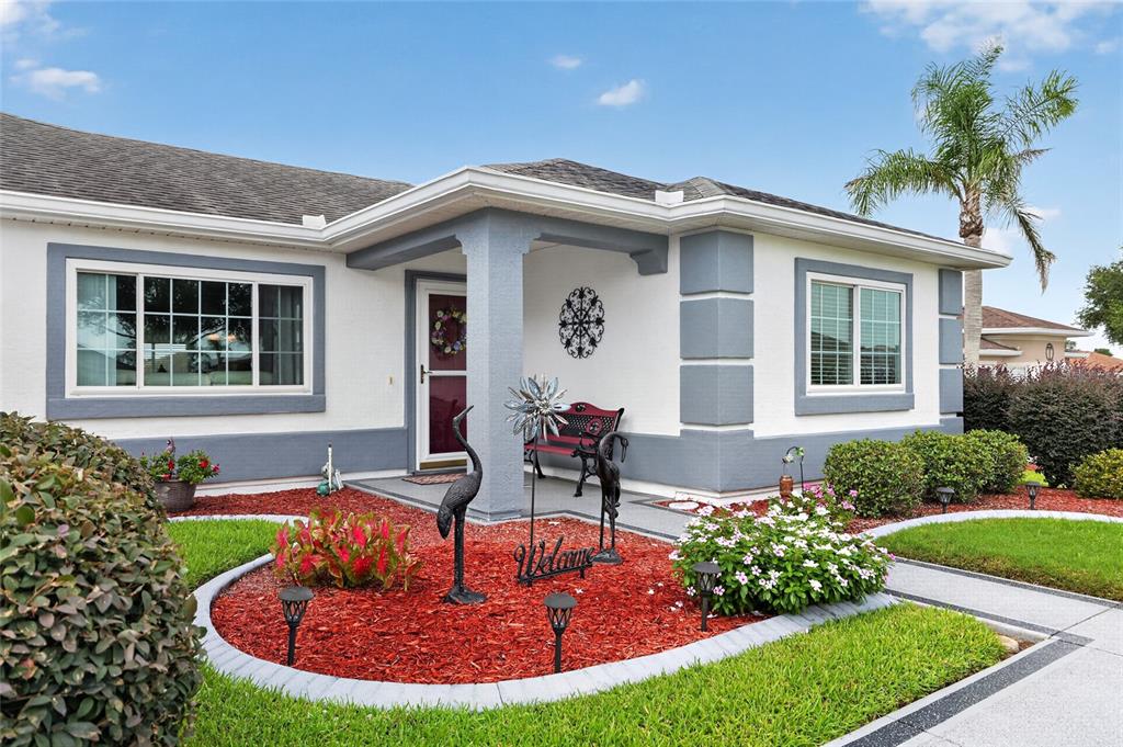 The exterior of a single-story house features white stucco walls, gray trim, and red mulch — 13600 SE 87TH CIRCLE, SUMMERFIELD, FL