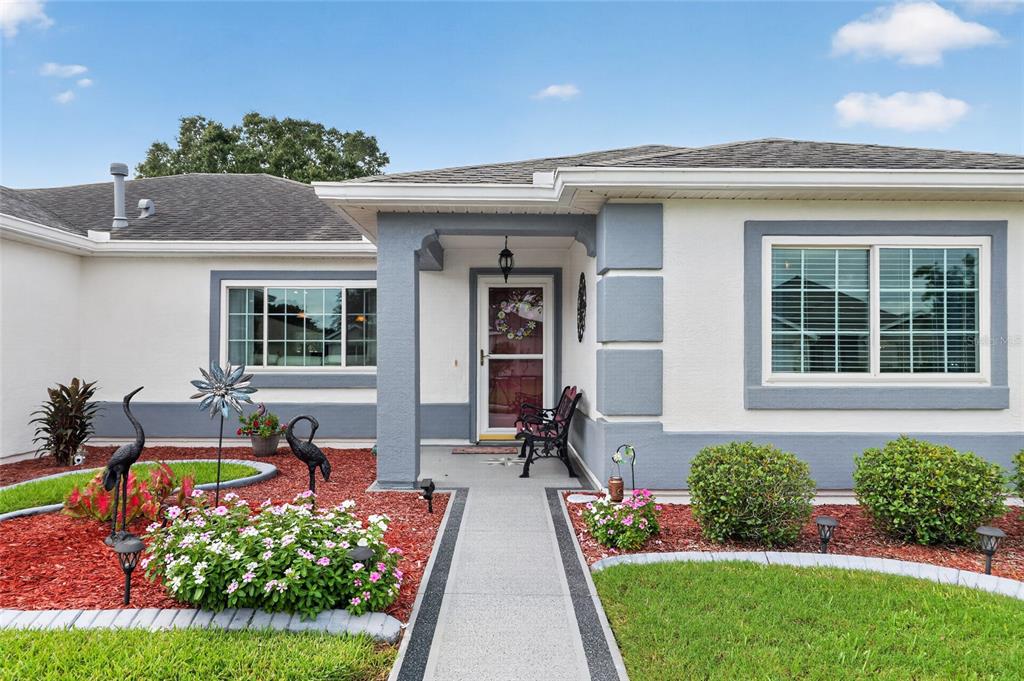 A single-story house exterior features a gray-trimmed entryway, a concrete walkway, and landscaped flower beds — 13600 SE 87TH CIRCLE, SUMMERFIELD, FL