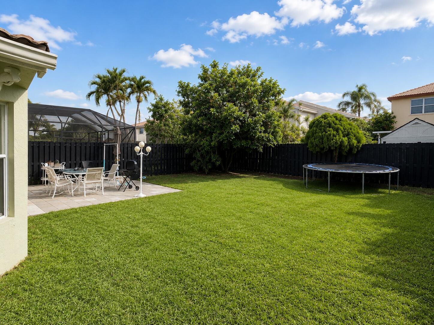 A backyard features a patio with outdoor furniture, a trampoline, and a black privacy fence — 7063 Middlebury Drive, Boynton Beach FL 33436, BOYNTON BEACH, FL