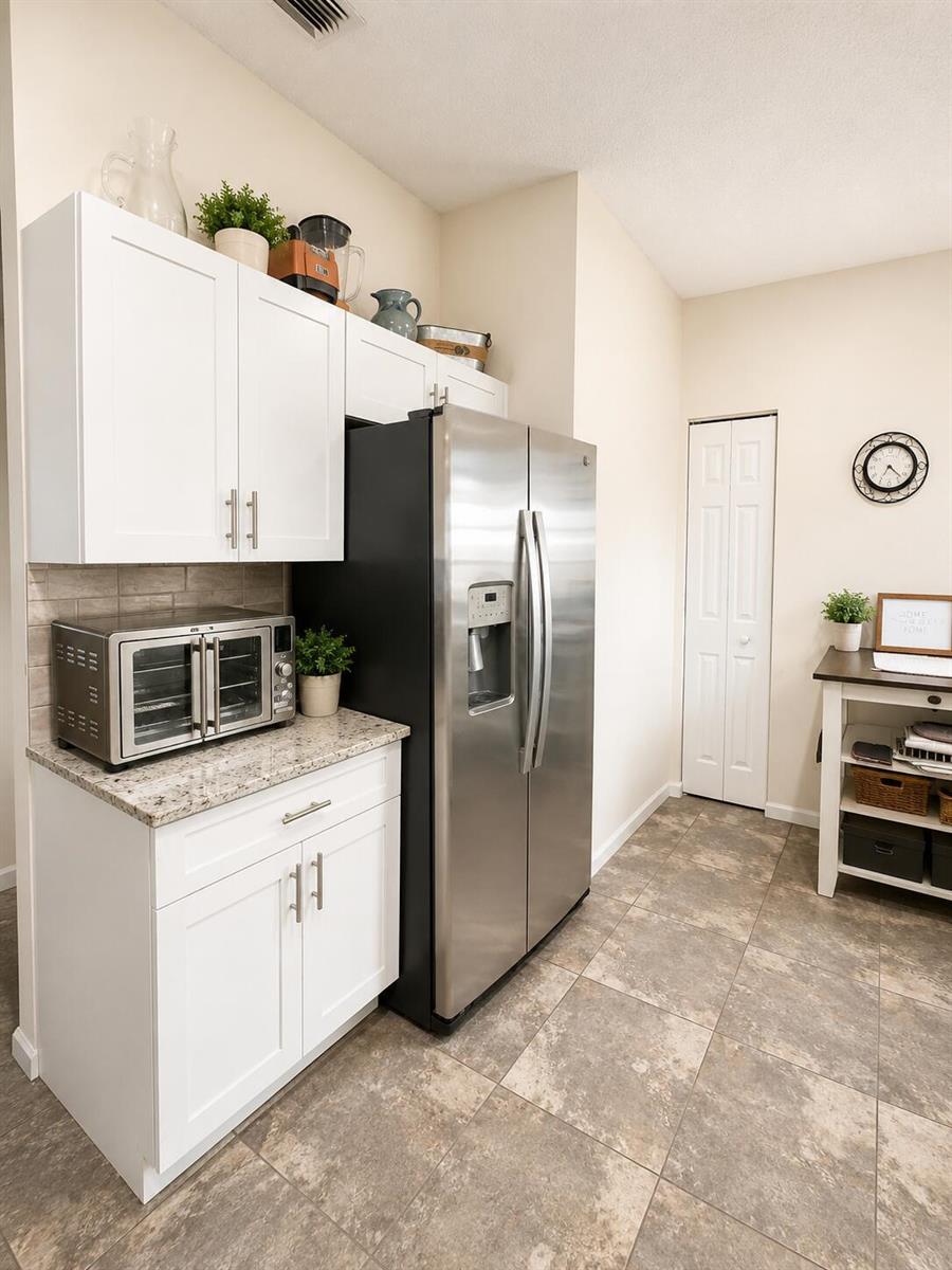 A kitchen features white cabinets, granite countertops, a stainless steel refrigerator, and tiled flooring — 7063 Middlebury Drive, Boynton Beach FL 33436, BOYNTON BEACH, FL
