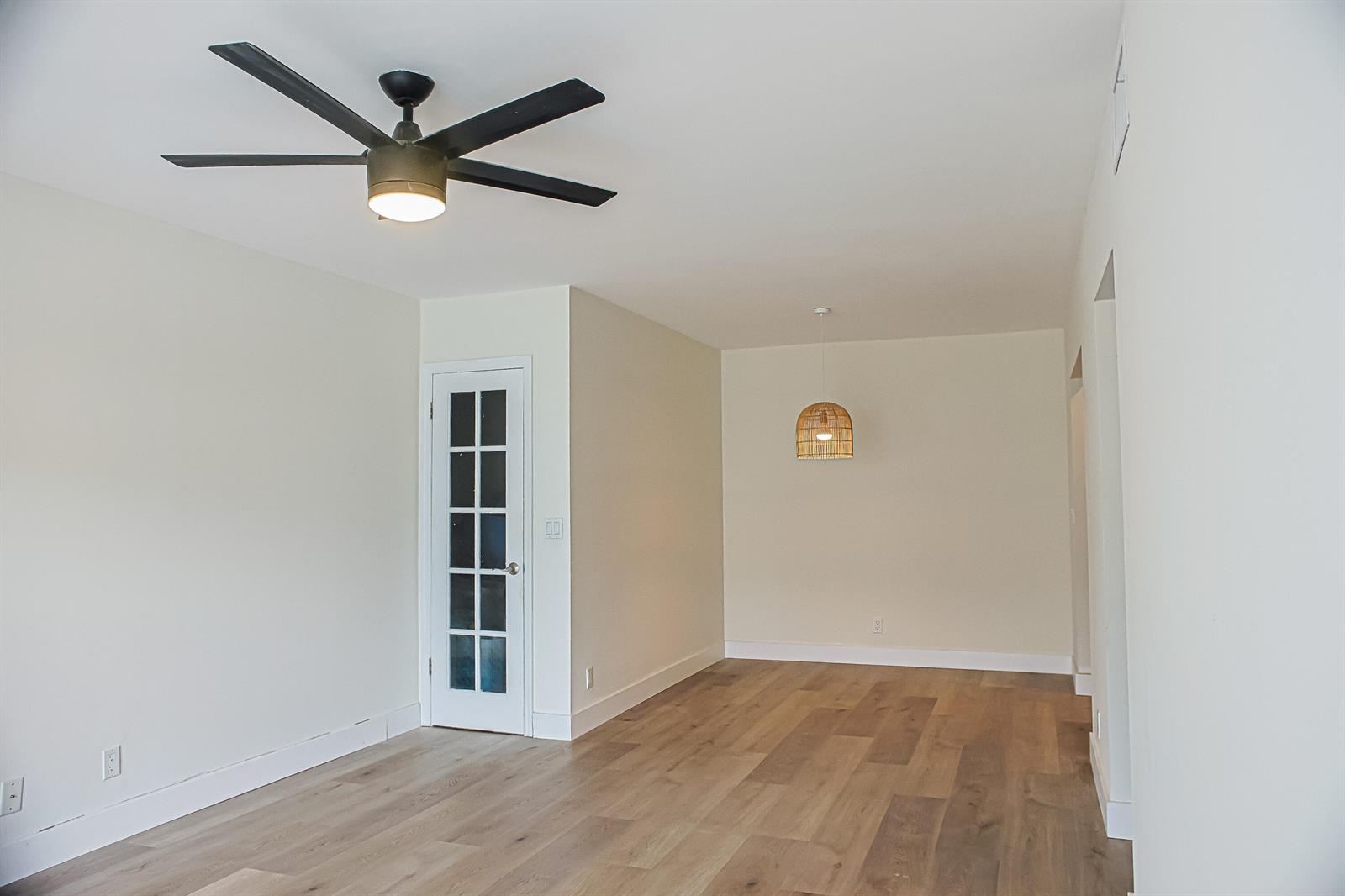 An empty room features light wood flooring, a black ceiling fan, and a hanging light fixture — 130 Cypress Club Drive # 309, Pompano Beach FL 33060, POMPANO BEACH, FL