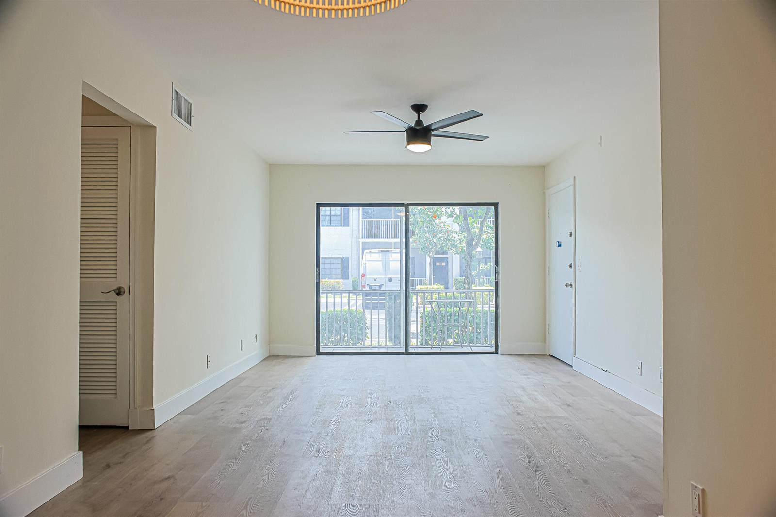 An empty living room features light wood-look flooring, a ceiling fan, and a sliding glass door — 130 Cypress Club Drive # 309, Pompano Beach FL 33060, POMPANO BEACH, FL