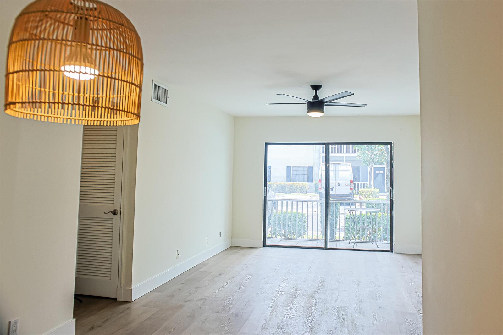 An empty room features light wood-look flooring, a ceiling fan, and a sliding glass door — 130 Cypress Club Drive # 309, Pompano Beach FL 33060, POMPANO BEACH, FL