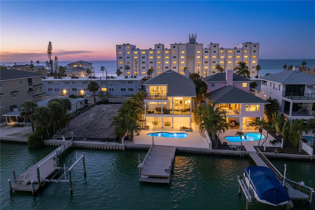 An aerial view of waterfront homes with private pools and docks at twilight — 8485 BLIND PASS DRIVE, TREASURE ISLAND, FL