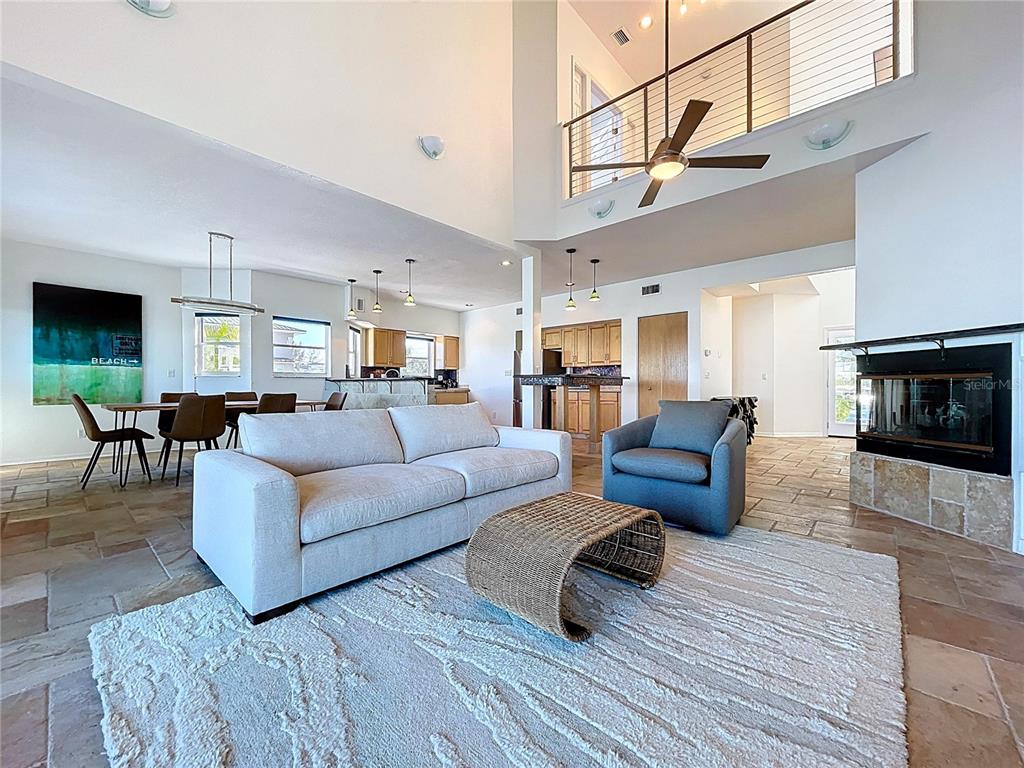 A living room with a high ceiling, stone tile floors, and an open kitchen area — 8485 BLIND PASS DRIVE, TREASURE ISLAND, FL