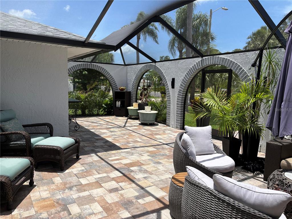 A screened-in patio features arched brick accents, tiled flooring, and outdoor wicker furniture — 5514 GRIDLEY LANE, NEW PORT RICHEY, FL