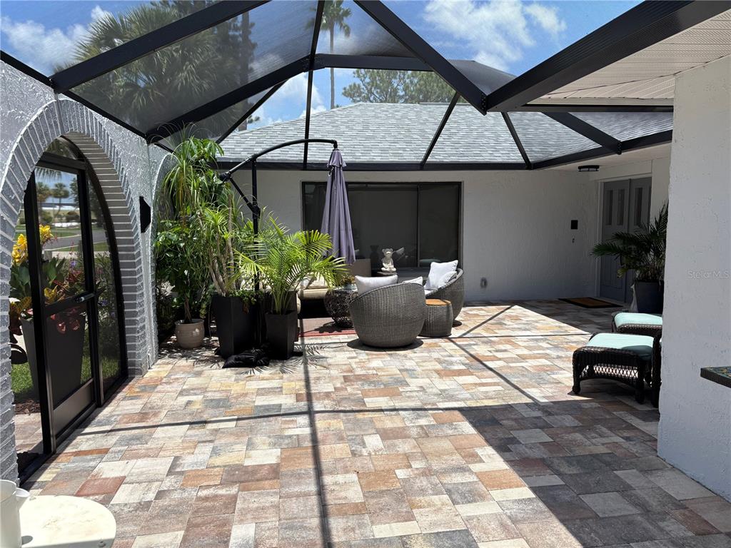 A screened-in patio features paver flooring, outdoor furniture, and potted plants under a roof — 5514 GRIDLEY LANE, NEW PORT RICHEY, FL