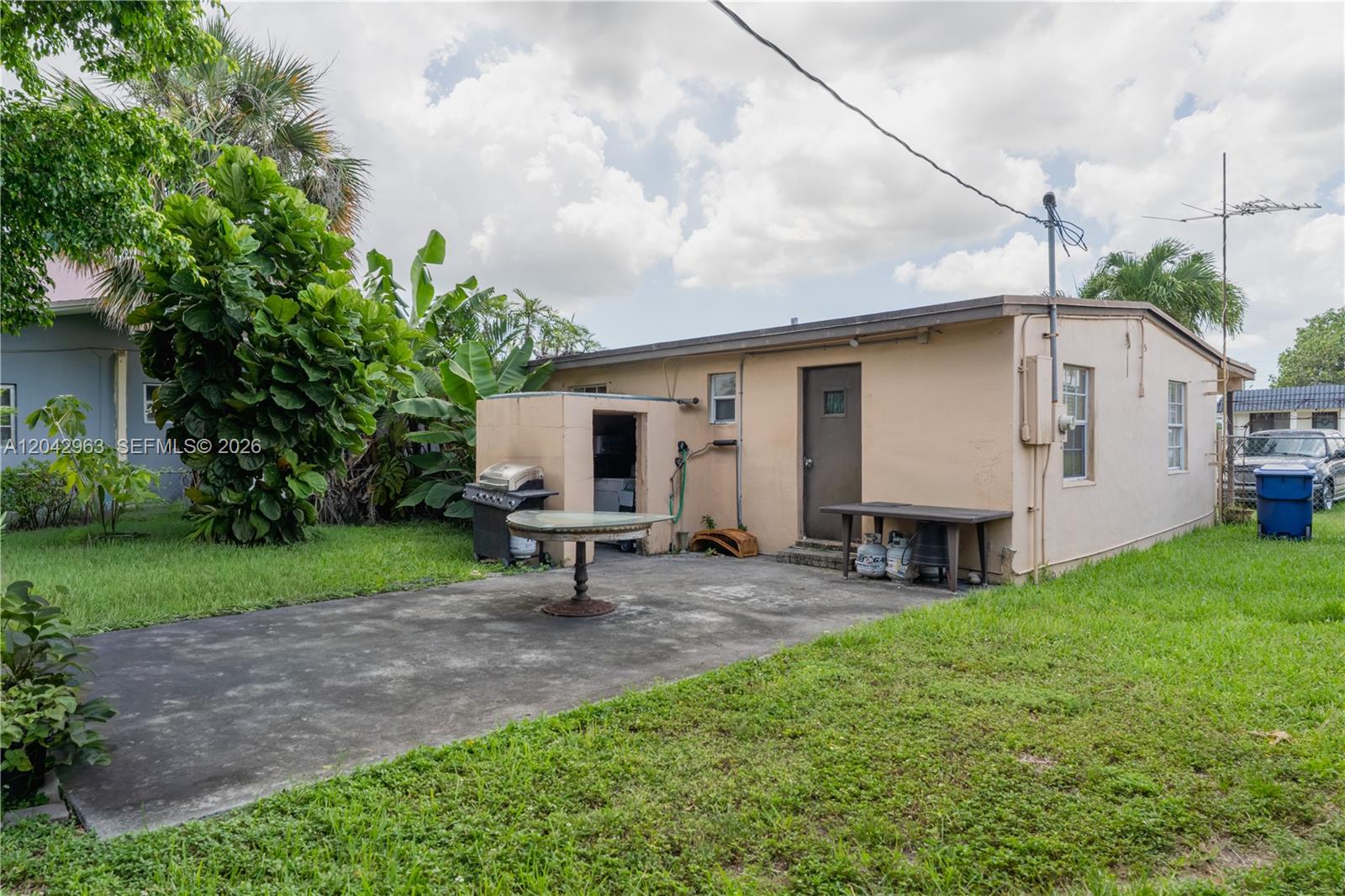 The exterior of a tan house features a concrete patio, a grill, and a table — 9265 SW 38th St, Miami FL 33165, MIAMI, FL