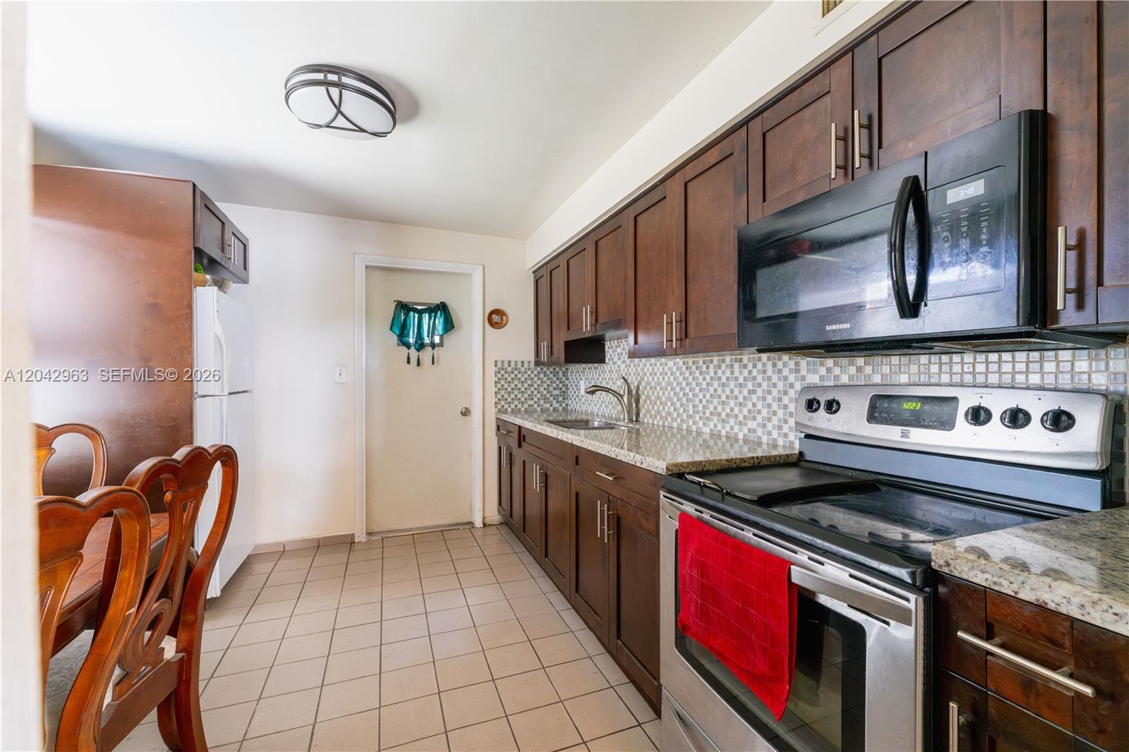 A kitchen features dark wood cabinets, granite countertops, stainless steel appliances, and tiled flooring — 9265 SW 38th St, Miami FL 33165, MIAMI, FL