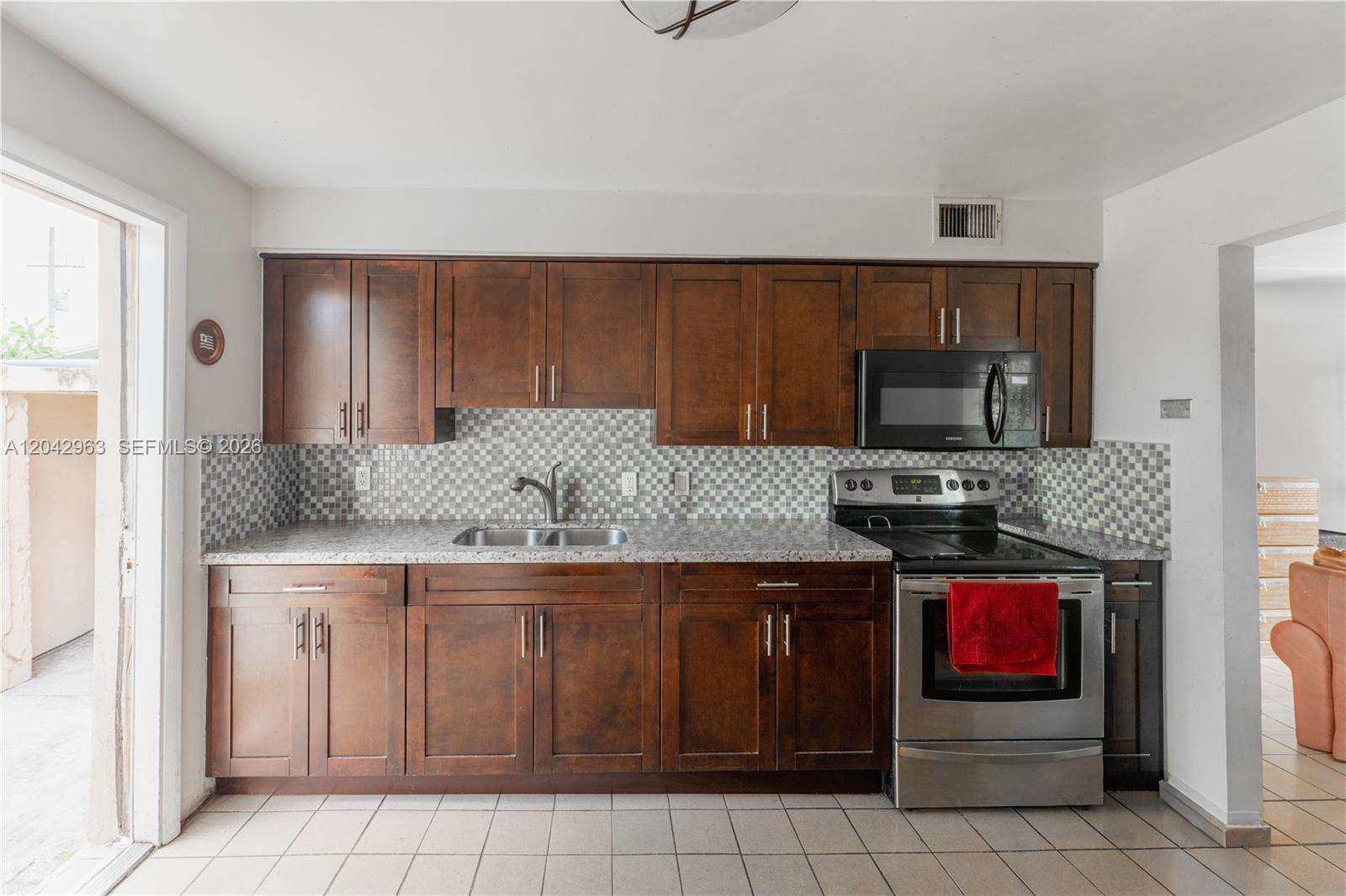 A kitchen features dark wood cabinets, granite countertops, a tiled backsplash, and stainless steel appliances — 9265 SW 38th St, Miami FL 33165, MIAMI, FL
