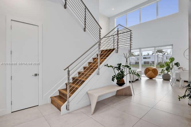 A modern staircase with wooden treads and a metal railing sits in a bright entryway — 10250 NW 75th Ter, Doral FL 33178, DORAL, FL