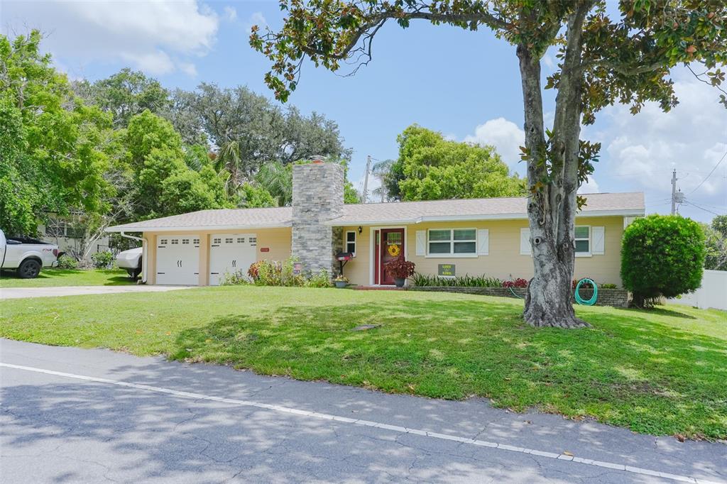 A single-story yellow house with a stone chimney, two-car garage, and a large front lawn — 3124 S POLK AVENUE, LAKELAND, FL