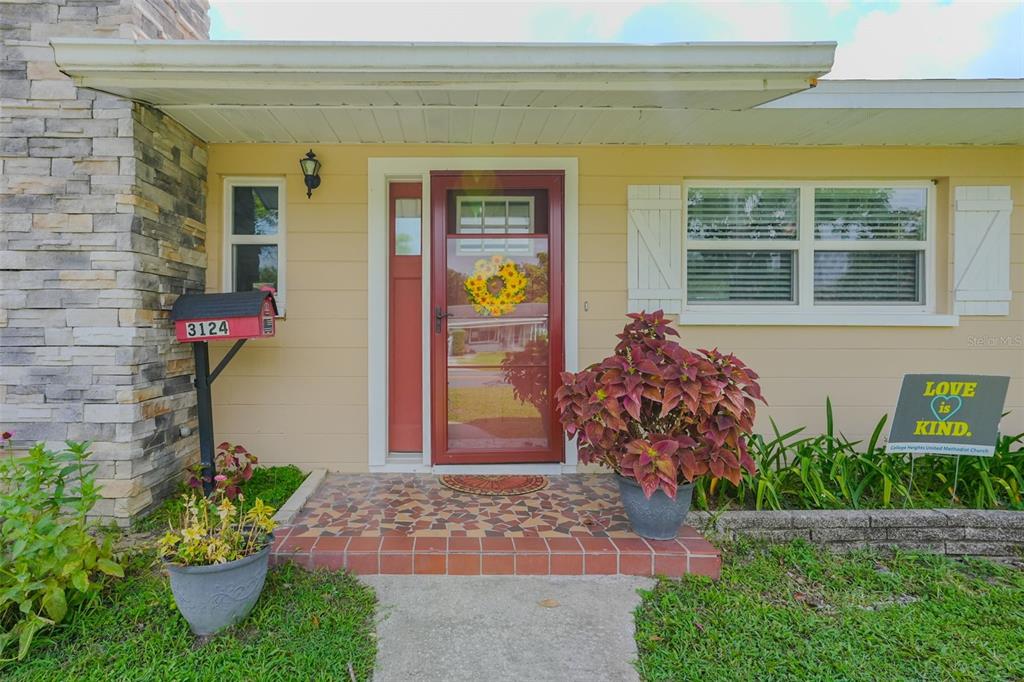 The front exterior of a house features a red door, stone siding, and a tiled porch — 3124 S POLK AVENUE, LAKELAND, FL