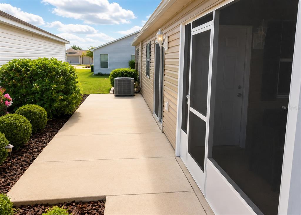 A concrete patio runs along the side of a house with tan siding and screens — 3463 PLACIDA TERRACE, THE VILLAGES, FL