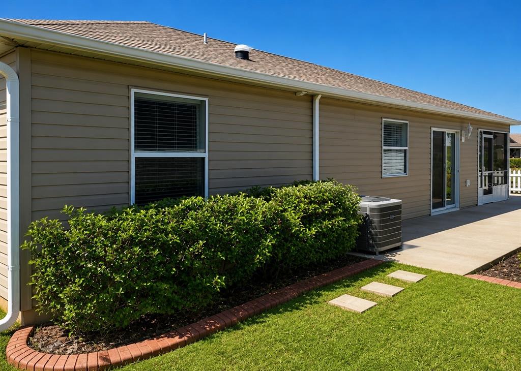 The exterior of a tan house features a concrete patio, landscaping, and an air conditioning unit — 3463 PLACIDA TERRACE, THE VILLAGES, FL