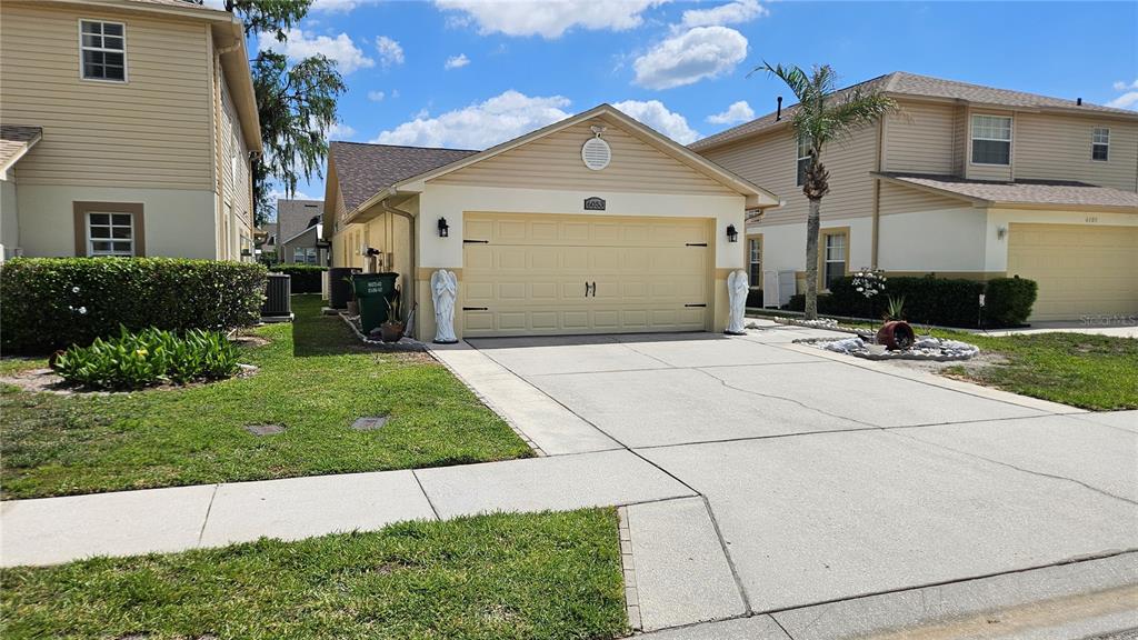 A beige suburban house with a two-car garage and a concrete driveway — 6053 GENTLE BEN CIRCLE, WESLEY CHAPEL, FL
