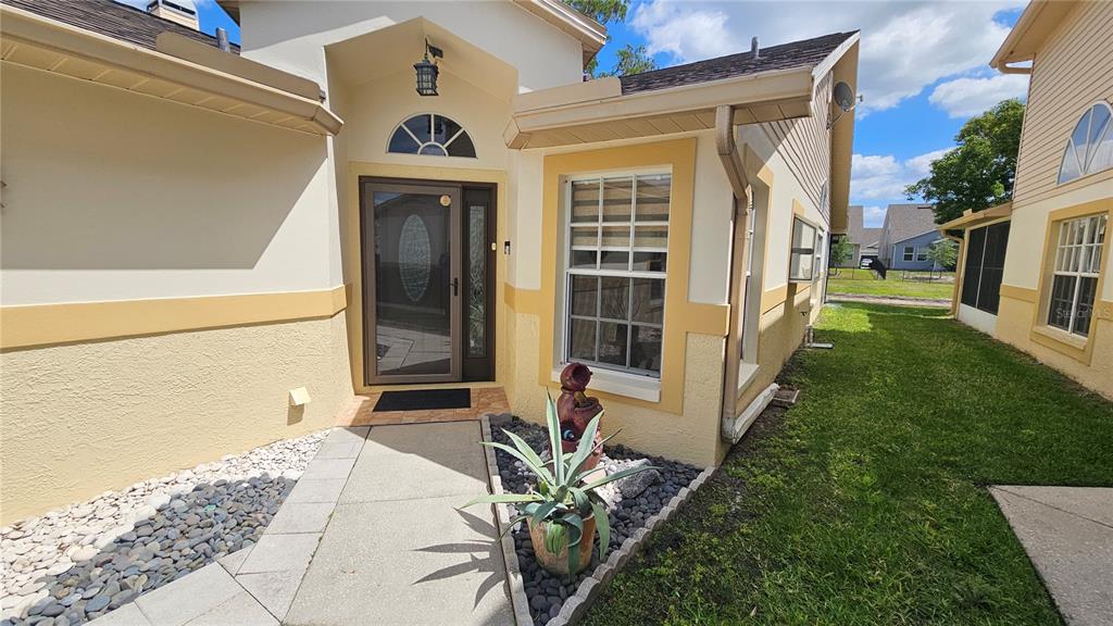 The exterior entrance of a house features a beige stucco facade, a walkway, and landscaping — 6053 GENTLE BEN CIRCLE, WESLEY CHAPEL, FL