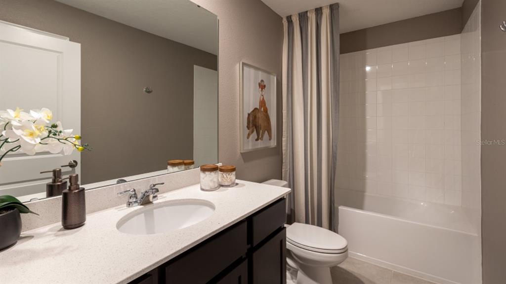 A bathroom features a white vanity, a mirror, a toilet, and a tiled shower-tub combo — 5240 WORCHESTER DRIVE, KISSIMMEE, FL