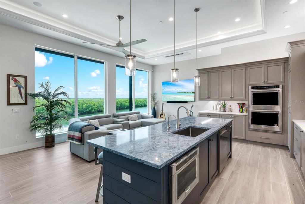 A modern kitchen with a blue island and gray sofa overlooks a lush green landscape — 5826 SHELL COVE DRIVE, CAPE CORAL, FL