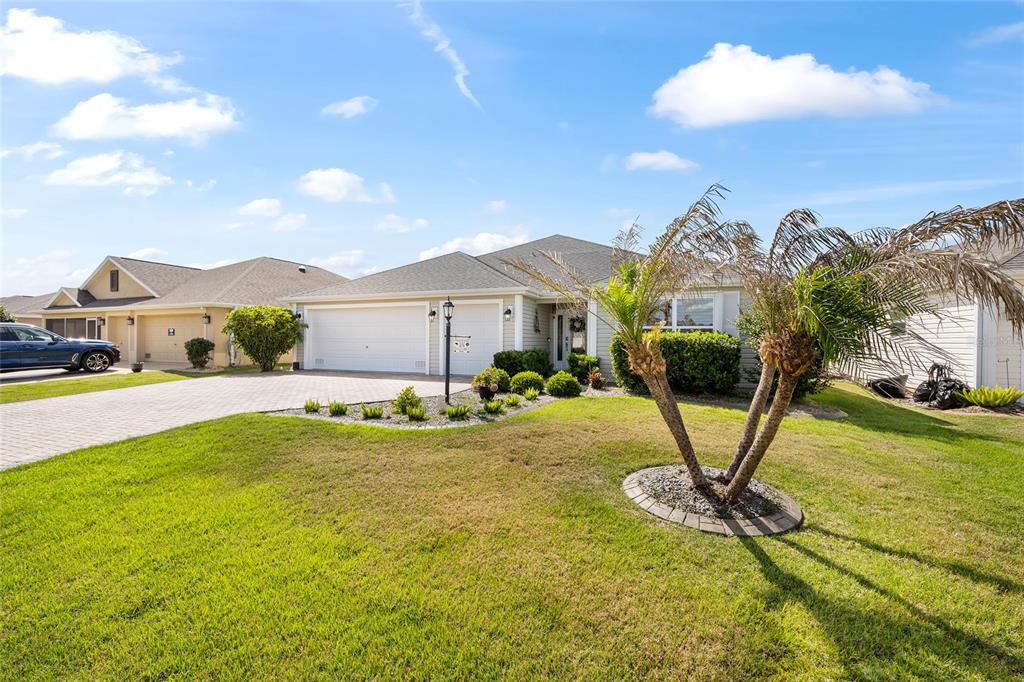 A single-story suburban house with a two-car garage, a paved driveway, and a palm tree — 475 ISLAND HOUSE PATH, THE VILLAGES, FL