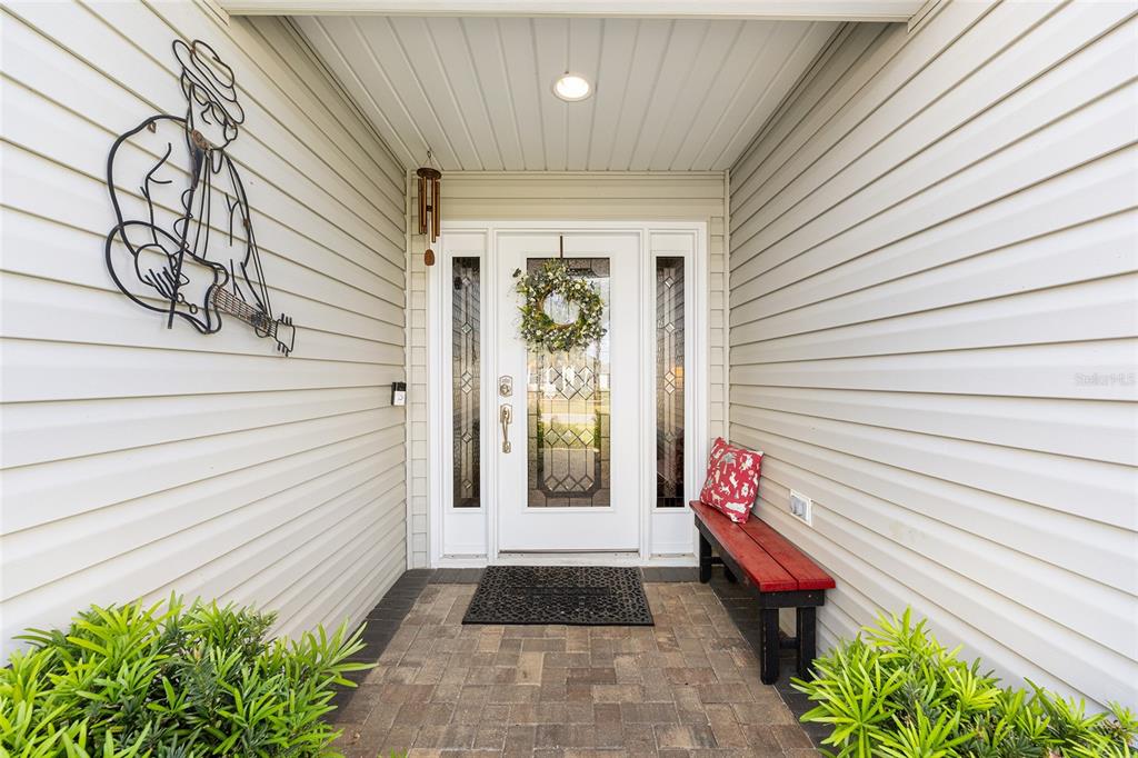A covered entryway features a white front door with glass panels, a bench, and wall decor — 475 ISLAND HOUSE PATH, THE VILLAGES, FL