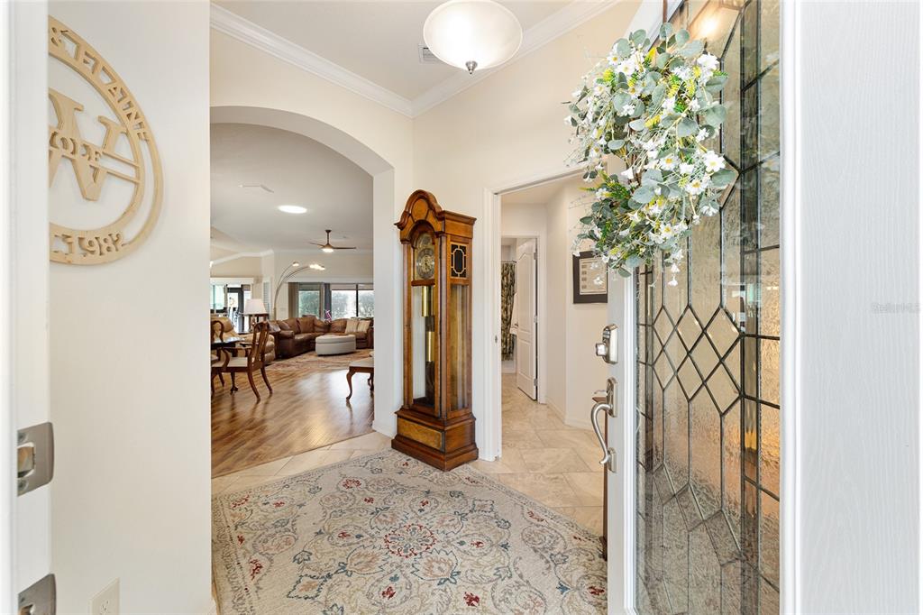 An entryway features a patterned rug, a grandfather clock, and a view into the living room — 475 ISLAND HOUSE PATH, THE VILLAGES, FL