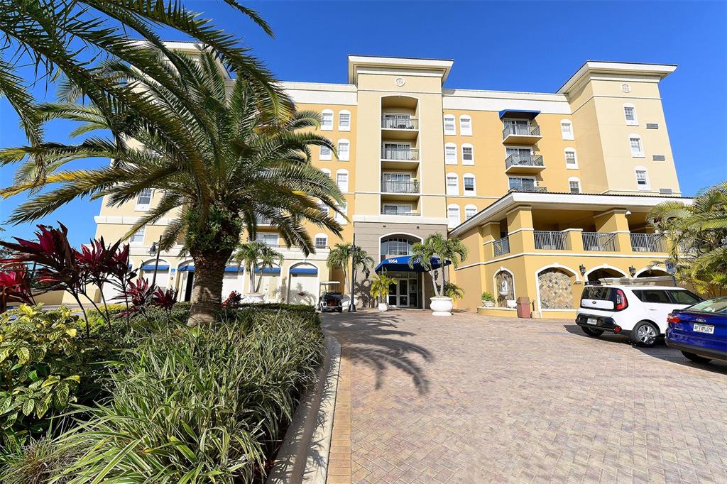 A multi-story yellow building with a paved driveway, palm trees, and parked cars in front — 1064 N TAMIAMI TRAIL UNIT 1627, SARASOTA, FL