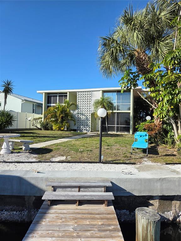 A two-story house with a white concrete block screen wall sits behind a wooden dock — 10215 MANATEE AVENUE W UNIT 1, BRADENTON, FL