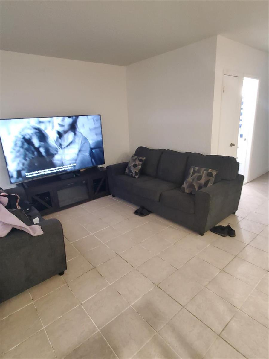 A living room features a dark gray sofa, a television on a stand, and tile flooring — 1021 NE 24th Avenue # 4, Pompano Beach FL 33062, POMPANO BEACH, FL
