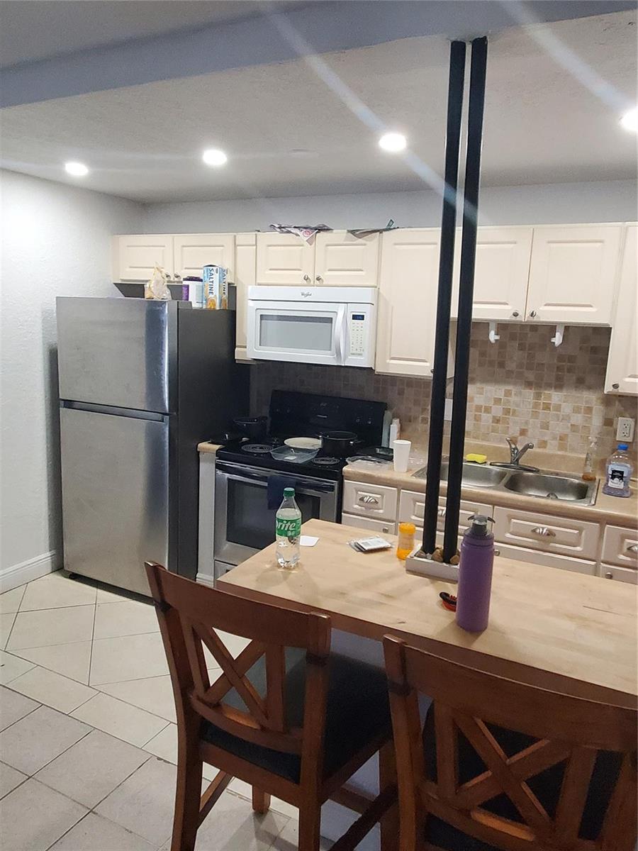 A kitchen features stainless steel appliances, cream-colored cabinets, a tile backsplash, and a wooden island — 1021 NE 24th Avenue # 4, Pompano Beach FL 33062, POMPANO BEACH, FL