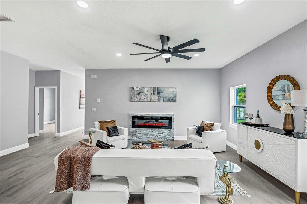 A living room features a fireplace, white furniture, a ceiling fan, and gray flooring — 721 INDIANA STREET, DAYTONA BEACH, FL