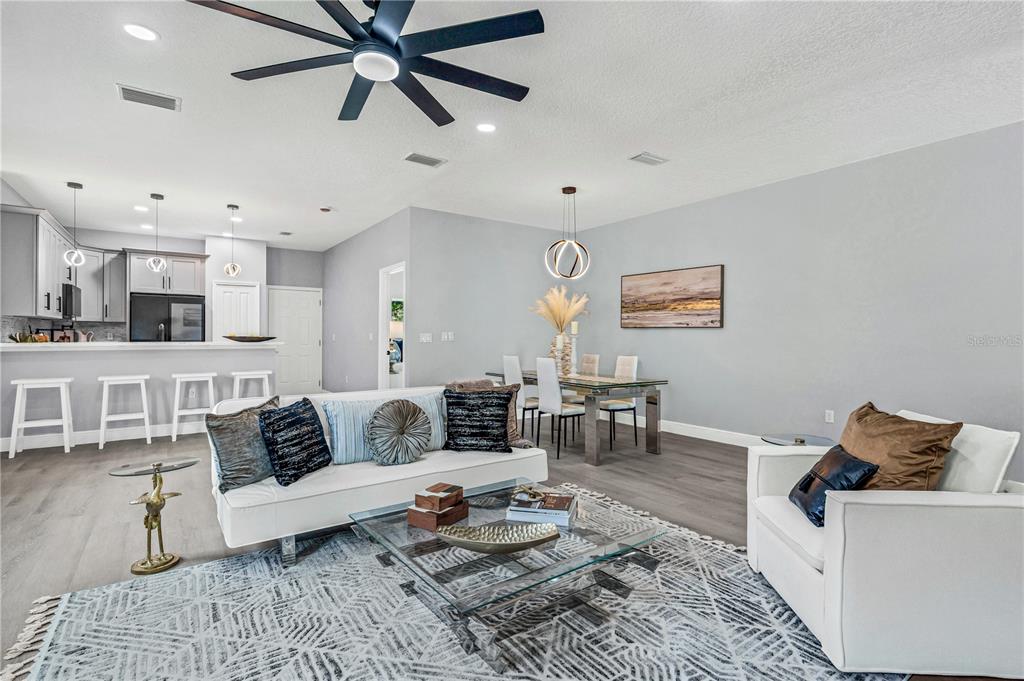 A modern open-concept living and dining area features gray wood flooring and white furniture — 721 INDIANA STREET, DAYTONA BEACH, FL
