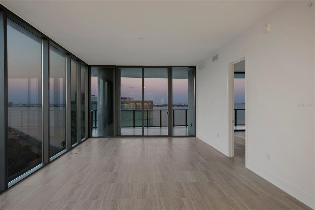 An empty room with light wood-look flooring, floor-to-ceiling windows, and a balcony overlooking water — 3015 S YSABELLA AVENUE UNIT 1601, TAMPA, FL