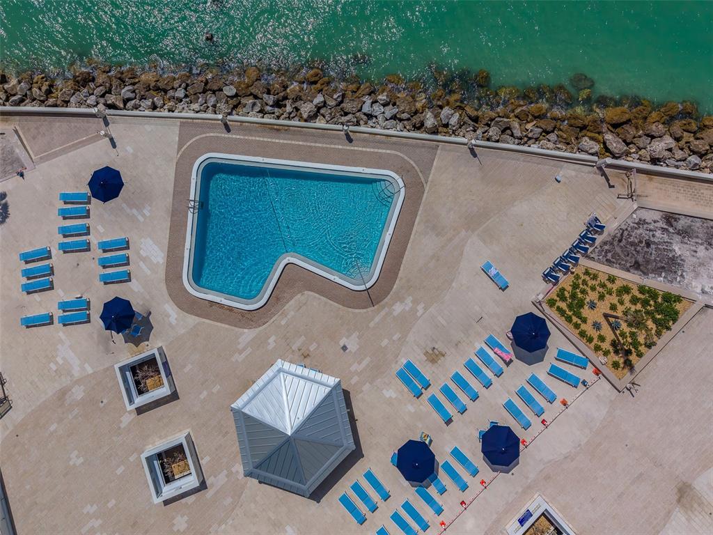 An aerial view shows a swimming pool, lounge chairs, umbrellas, and a gazebo by water — 450 S GULFVIEW BOULEVARD UNIT 208, CLEARWATER BEACH, FL