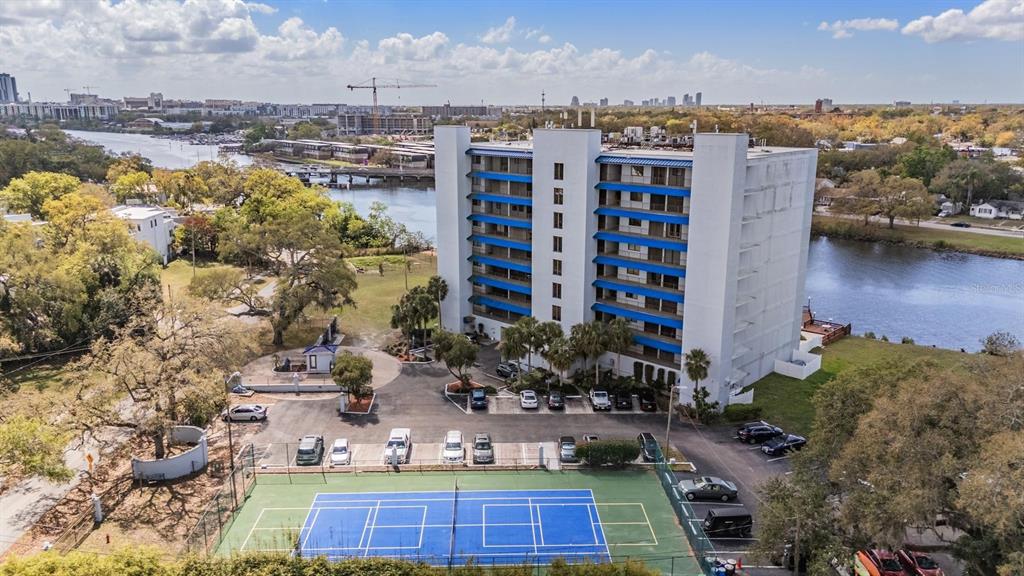 An aerial view shows a multi-story apartment building with a tennis court and parking lot — 2780 N RIVERSIDE DRIVE UNIT 105, TAMPA, FL