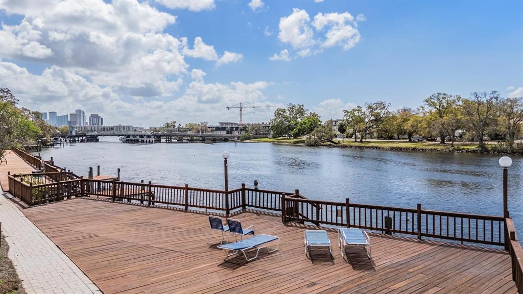 A wooden deck with lounge chairs overlooks a river with a bridge in the distance — 2780 N RIVERSIDE DRIVE UNIT 105, TAMPA, FL