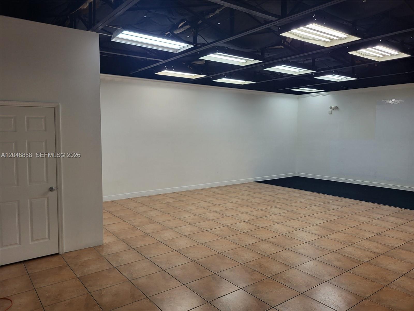 An empty room features tiled flooring, white walls, and exposed ceiling lights — 2223 NW 26th Ave, Miami FL 33142, MIAMI, FL