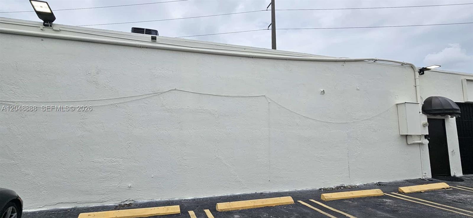 A plain white exterior wall of a commercial building features parking spaces with yellow bumpers — 2223 NW 26th Ave, Miami FL 33142, MIAMI, FL