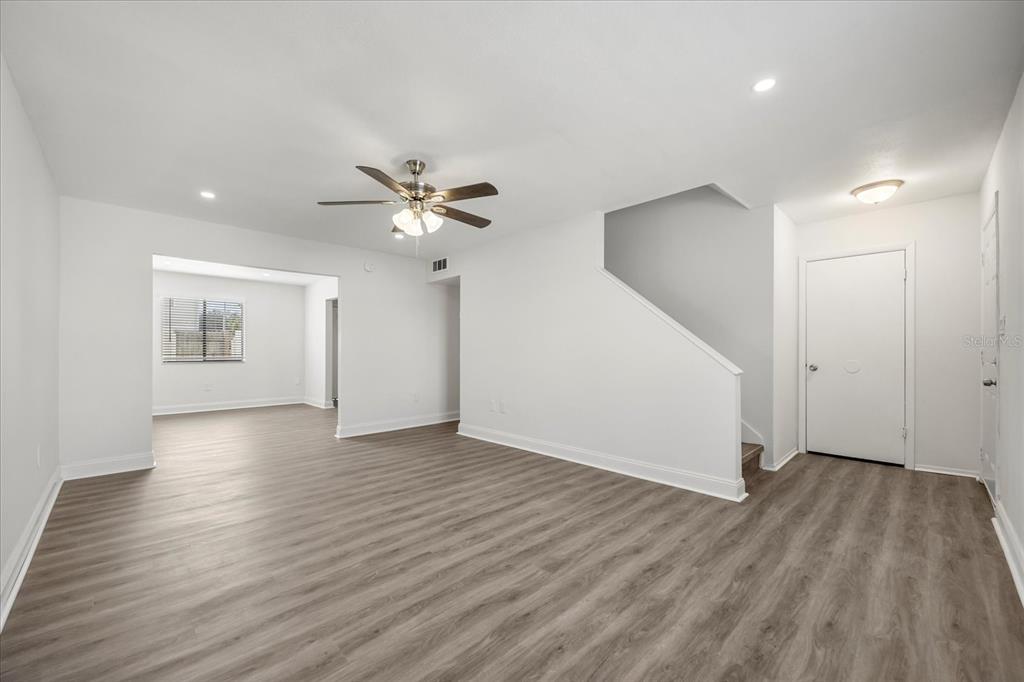 An empty living room features white walls, light wood-look flooring, a ceiling fan, and stairs — 217 DEBORA COURT, ALTAMONTE SPRINGS, FL