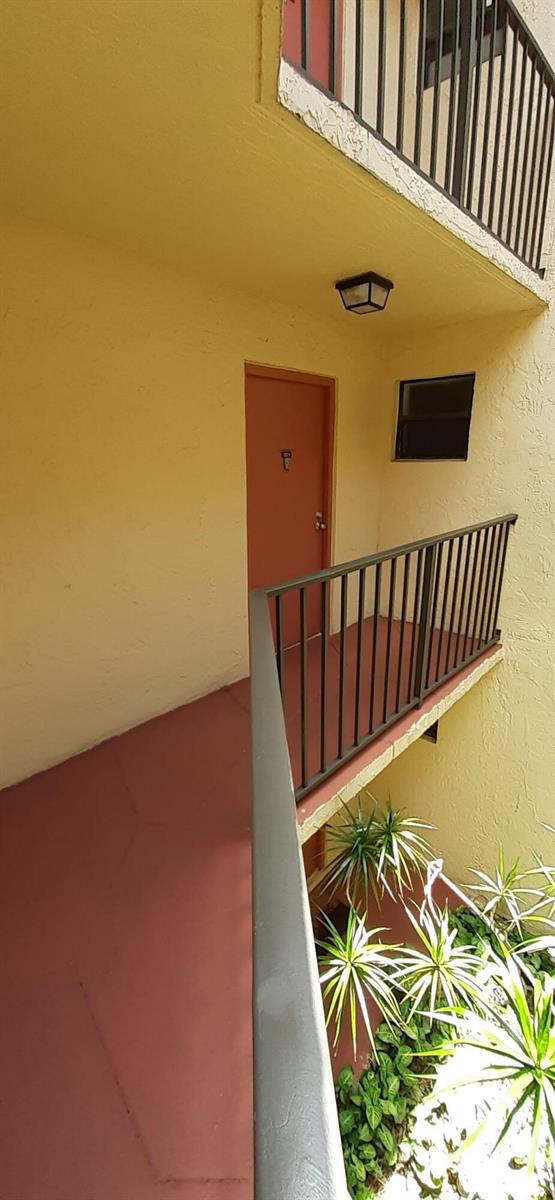 An exterior view of an apartment building walkway with a red door and metal railings — 3252 Foxcroft Road # 201, Miramar FL 33025, MIRAMAR, FL