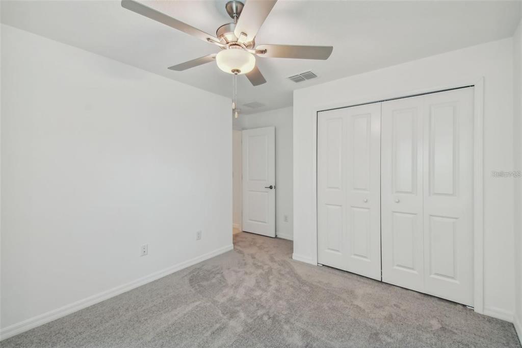 A bedroom with white walls, gray carpeting, a ceiling fan, and white closet doors — 9828 BRANCHING SHIP TRACE, WESLEY CHAPEL, FL