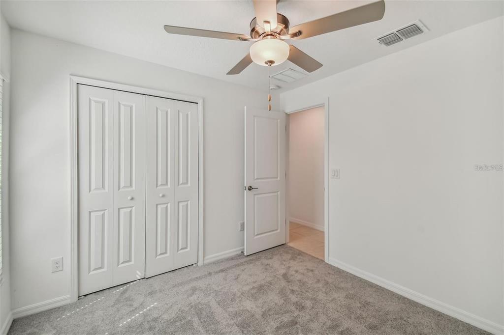 A bedroom features gray carpet, white walls, a ceiling fan, and a closet with doors — 9828 BRANCHING SHIP TRACE, WESLEY CHAPEL, FL