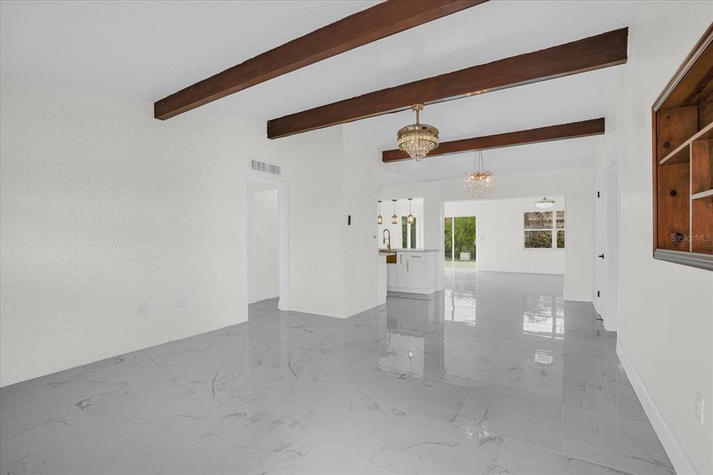 A bright, open-concept living area features white brick walls, dark wood ceiling beams, and tile — 290 PATRICK AVENUE, MERRITT ISLAND, FL