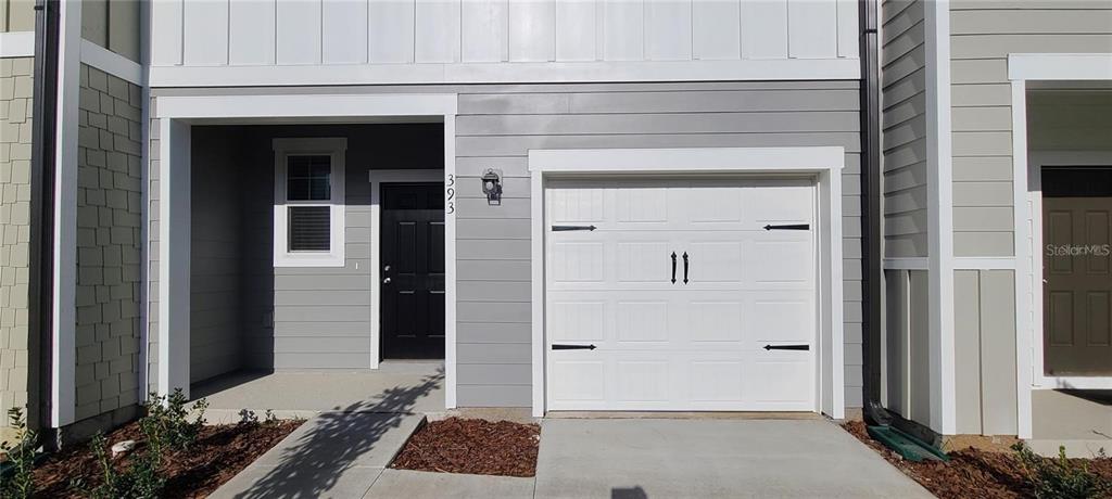 A gray townhouse exterior features a white garage door, a black front door, and siding — 393 MADISON DRIVE, DAVENPORT, FL