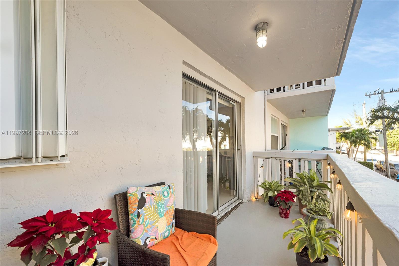 A balcony features a wicker chair, potted plants, string lights, and a sliding glass door — 7620 Carlyle Ave # 204, Miami Beach FL 33141, MIAMI BEACH, FL