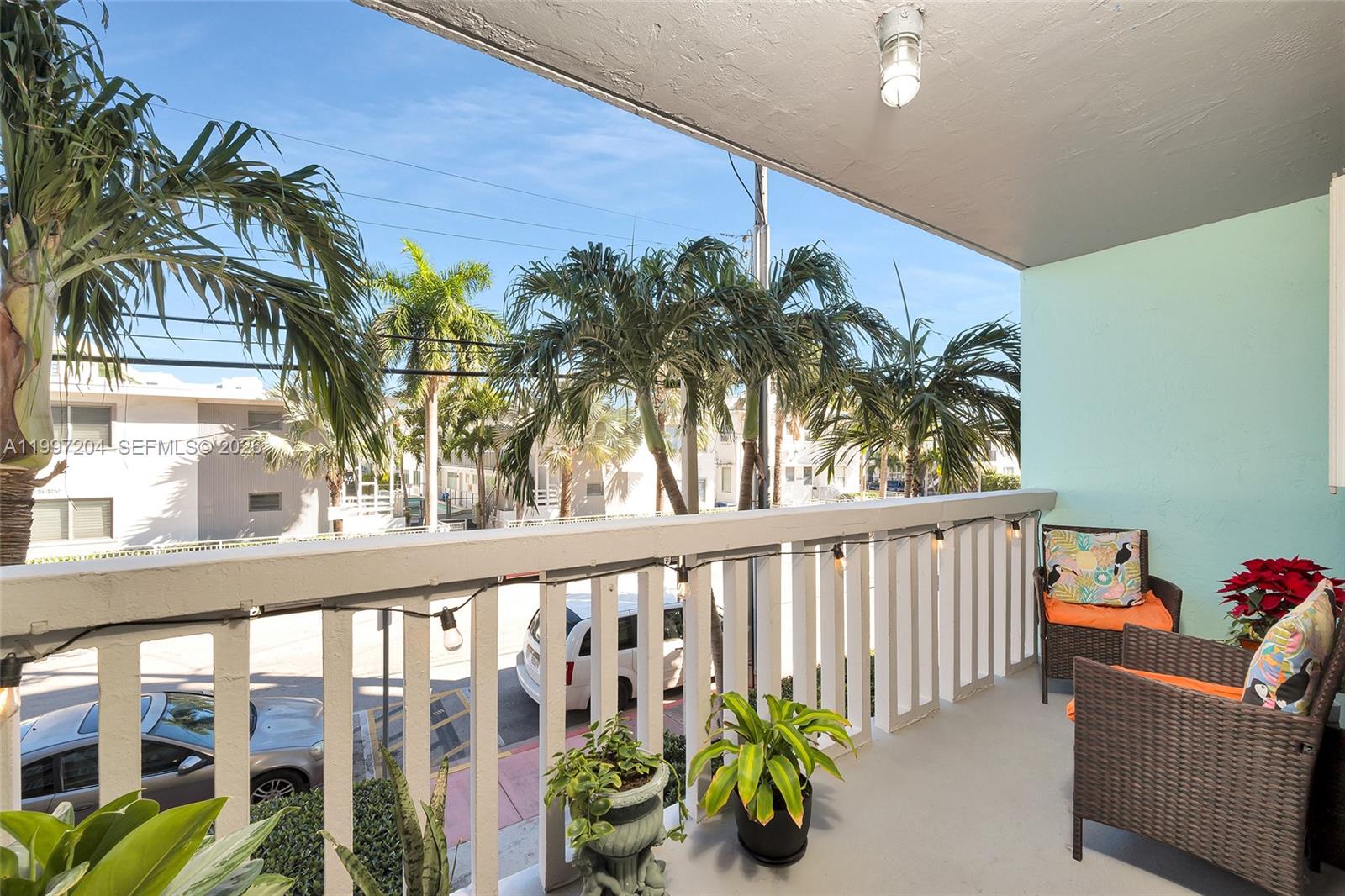 A balcony features wicker chairs, potted plants, string lights, and a view of palm trees — 7620 Carlyle Ave # 204, Miami Beach FL 33141, MIAMI BEACH, FL