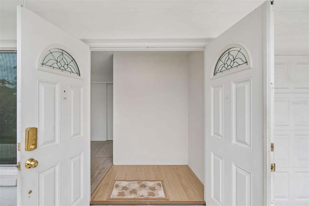 An open double front door reveals a small entryway with wood-look flooring and carpeted interior — 14142 90TH AVENUE, SEMINOLE, FL