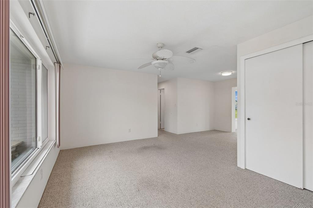 A carpeted bedroom features a ceiling fan, a large window, and a white sliding closet door — 14142 90TH AVENUE, SEMINOLE, FL