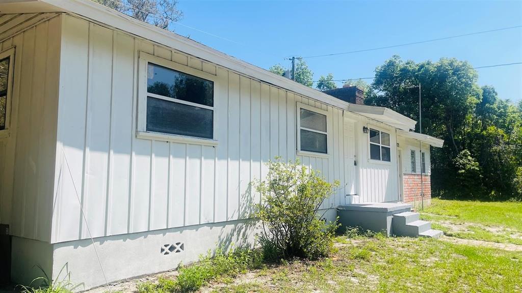 A white house with vertical siding and a brick accent wall under a clear sky — 703 GOTTS ROAD, DAVENPORT, FL