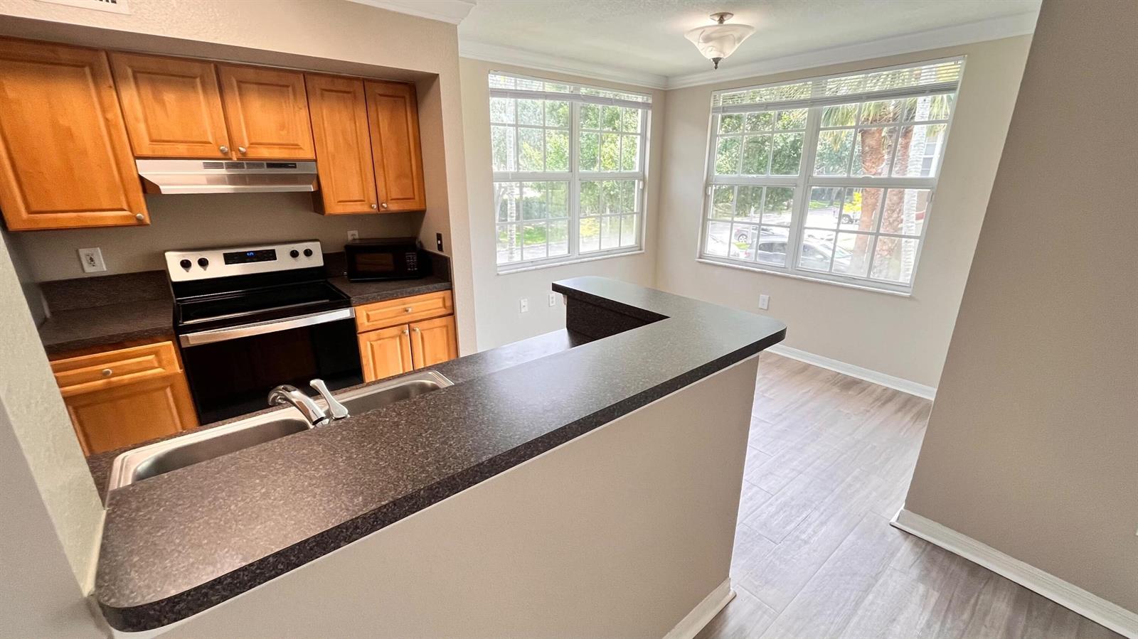 A kitchen with wood cabinets, dark countertops, and a breakfast bar overlooking a dining area — 15035 Michelangelo 202 Boulevard # 202, Delray Beach FL 33446, DELRAY BEACH, FL